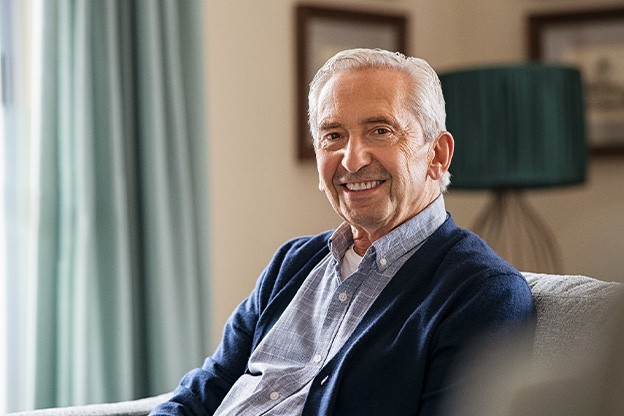 Senior man in button-up shirt sitting on couch and smiling