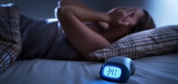 Woman lying awake in bed with alarm clock in foreground