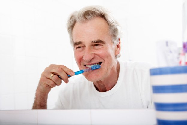 Senior man smiling and brushing his teeth